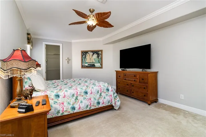 Carpeted bedroom with crown molding, a ceiling fan, and a spacious closet