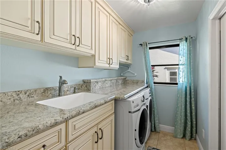 Laundry area featuring washer and dryer, light tile patterned floors, cabinets, and sink