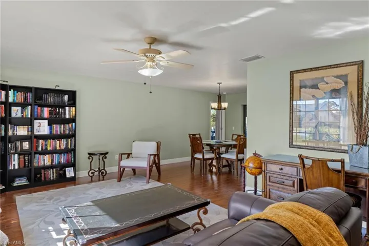 Living room featuring ceiling fan with notable chandelier and dark wood-type flooring