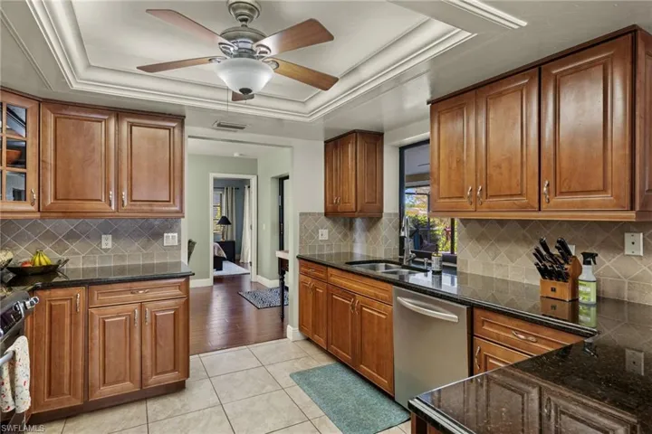 Kitchen with a raised ceiling, decorative backsplash, dark stone countertops, light tile patterned flooring, and stainless steel appliances