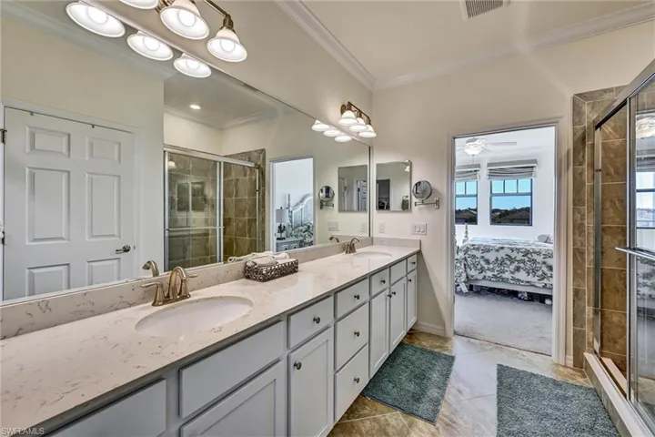 Ensuite bathroom featuring a stall shower, double vanity, and ornamental molding