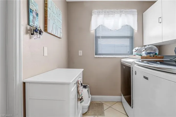 Clothes washing area featuring washer and dryer, cabinets, and light tile floors