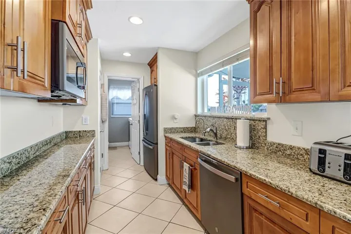 Kitchen featuring stainless steel appliances, light stone counters, sink, and light tile floors