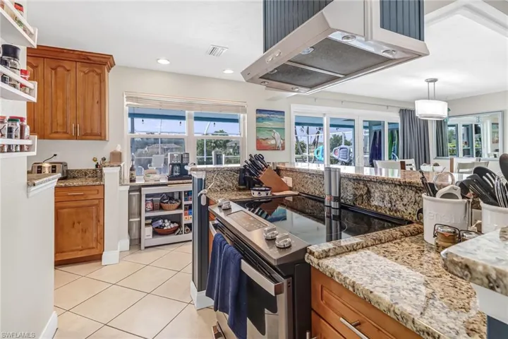 Kitchen featuring decorative light fixtures, stainless steel electric stove, light tile flooring, and light stone countertops