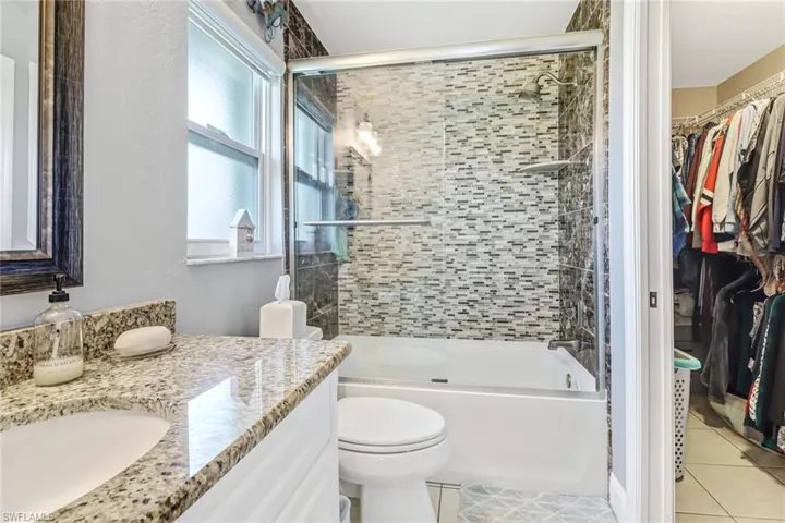 Full bathroom with tile floors, oversized vanity, toilet, and bath / shower combo with glass door