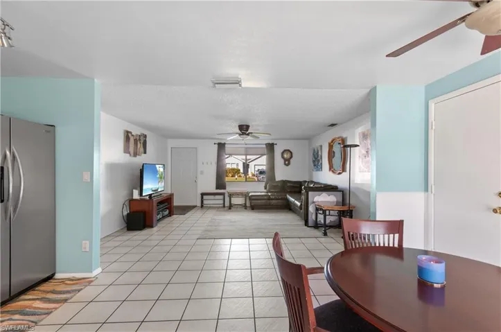 Open-concept interior featuring light-colored floor tiling, dual ceiling fans, and a stainless steel refrigerator