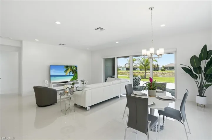 Open-concept interior featuring large-format tile flooring, recessed lighting, a multi-pane sliding glass door, and a five-light polished metal chandelier