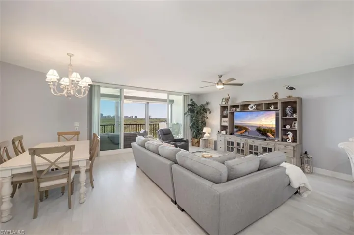 Living room with light wood finished floors, ceiling fan, a chandelier, and expansive windows