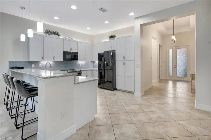 Kitchen with white cabinetry, kitchen peninsula, backsplash, a breakfast bar, and black appliances