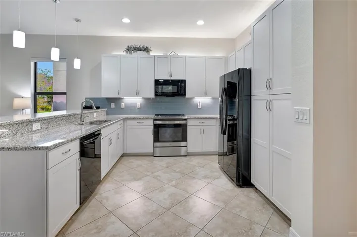Kitchen with black appliances, decorative light fixtures, white cabinetry, decorative backsplash, and light stone counters