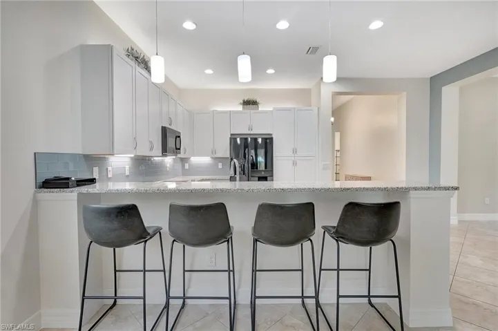 Kitchen featuring black appliances, kitchen peninsula, decorative backsplash, white cabinetry, and light stone counters