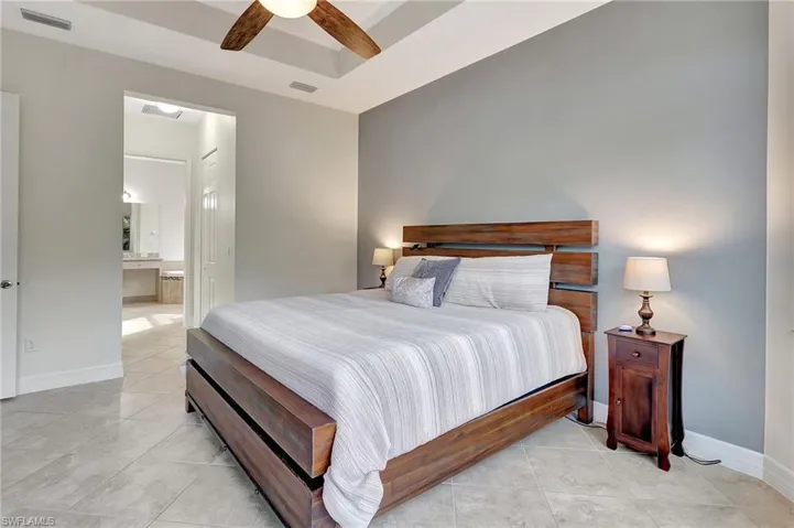 Tiled bedroom with ceiling fan, ensuite bathroom, and a tray ceiling