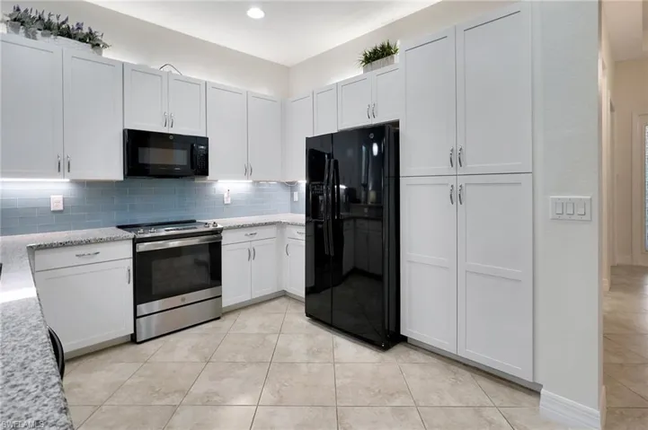 Kitchen with black appliances, decorative backsplash, and white cabinetry