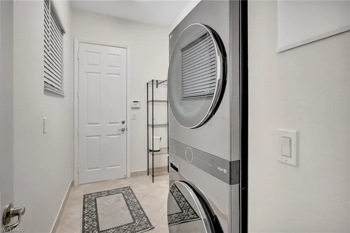 Clothes washing area featuring stacked washing maching and dryer and light tile patterned floors
