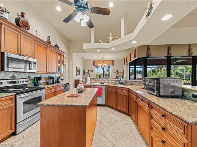 Kitchen with brown cabinets, stainless steel appliances, a center island, tasteful backsplash, and a chandelier