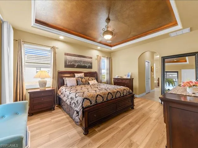 Bedroom featuring a tray ceiling, light wood-style floors, arched walkways, and a textured ceiling