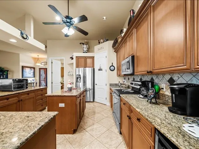 Kitchen featuring appliances with stainless steel finishes, brown cabinets, light stone countertops, light tile patterned flooring, and decorative backsplash