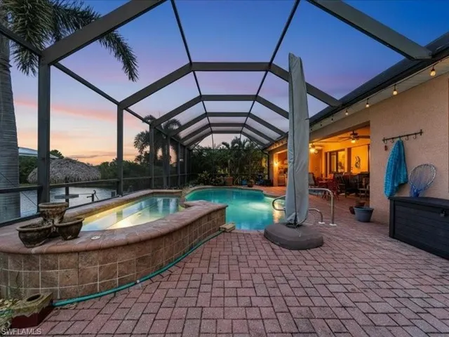 Pool at dusk with a sunroom, glass enclosure, a pool with connected hot tub, and a patio