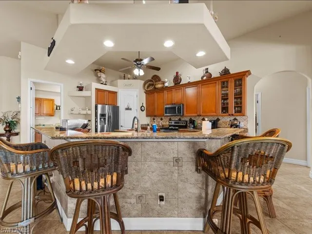 Kitchen with a kitchen breakfast bar, tasteful backsplash, appliances with stainless steel finishes, arched walkways, and dark stone counters