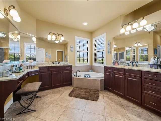 Full bathroom featuring a garden tub, two vanities, light tile patterned flooring, and recessed lighting