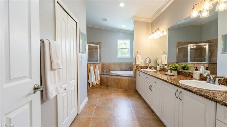 Dual-sink vanity with stone-finish countertops, soaking tub with tile surround, walk-in shower, and crown molding