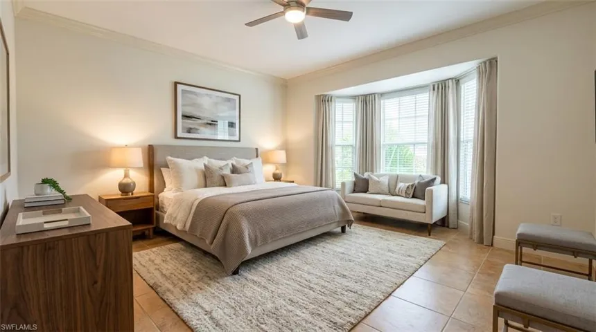 Neutral-toned room featuring a bay window, crown molding, ceiling fan with integrated lighting, and tile flooring