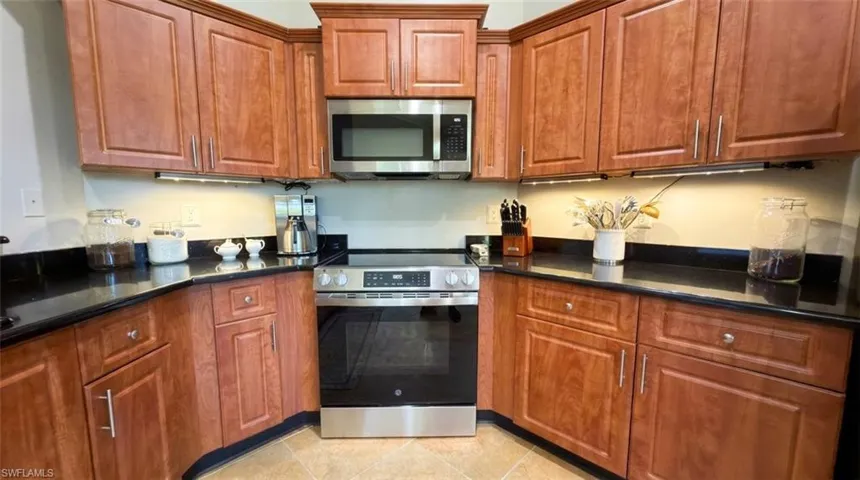 Kitchen featuring wood cabinetry, dark stone countertops, stainless steel electric range, stainless steel microwave, and under-cabinet lighting