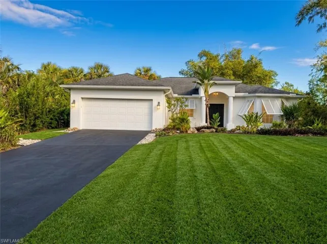 Stucco exterior featuring an arched entryway with columns, a two-car garage, white louvered window shutters, and a manicured lawn