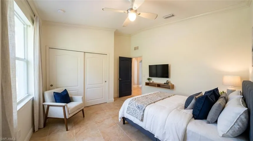 Neutral-toned room featuring large-format tile flooring, high ceilings, crown molding, a central ceiling fan, and sliding closet doors