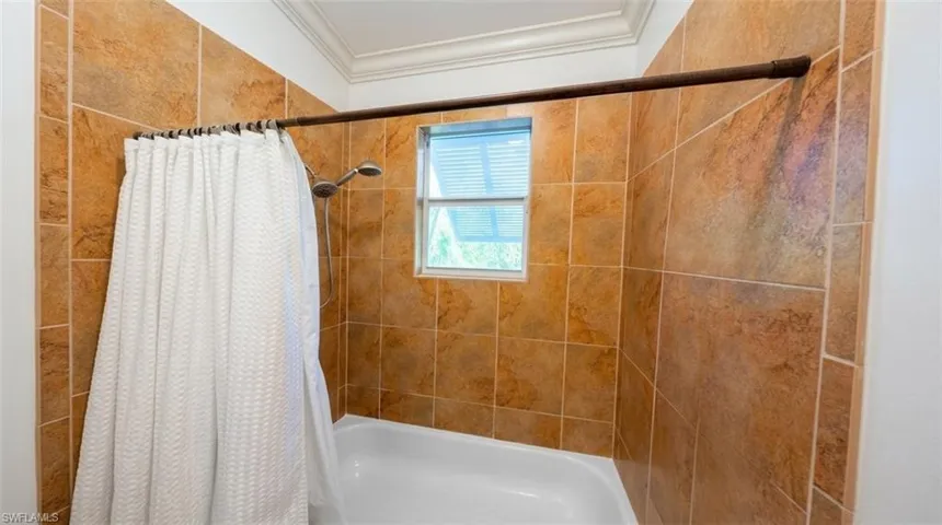 Shower area featuring floor-to-ceiling textured tile surround, a built-in tub, a wall-mounted showerhead, and a fixed window with integrated blinds
