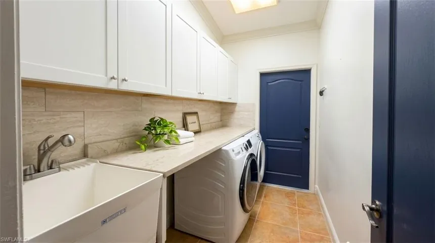 Laundry room featuring white shaker-style cabinetry, a stone-finish countertop, a deep utility sink with a pull-down faucet, and neutral-toned tile flooring