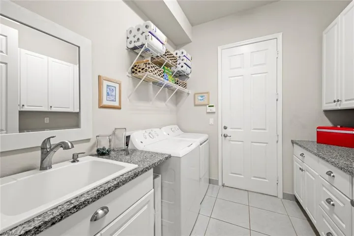 Laundry room featuring light tile patterned flooring, a sink, baseboards, washer and dryer, and cabinet space