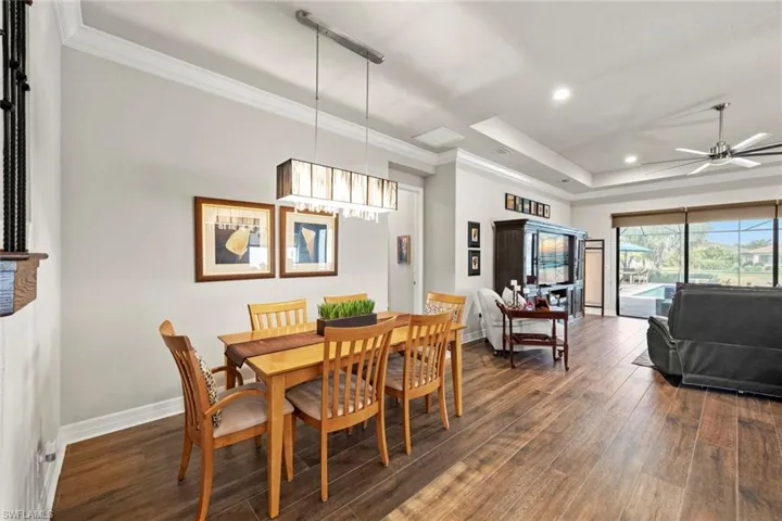 Dining space featuring baseboards, ceiling fan, dark wood-style flooring, a tray ceiling, and crown molding