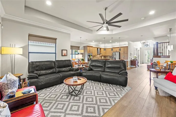 Living area featuring recessed lighting, ceiling fan with notable chandelier, light wood-style floors, a raised ceiling, and crown molding