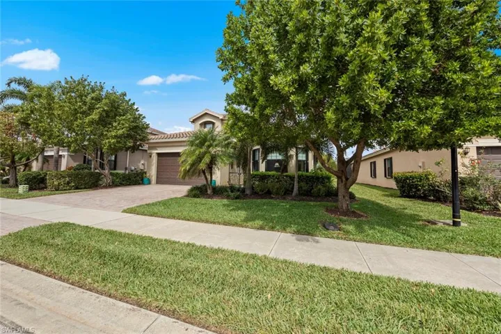 View of property hidden behind natural elements featuring a garage, a front yard, decorative driveway, and stucco siding