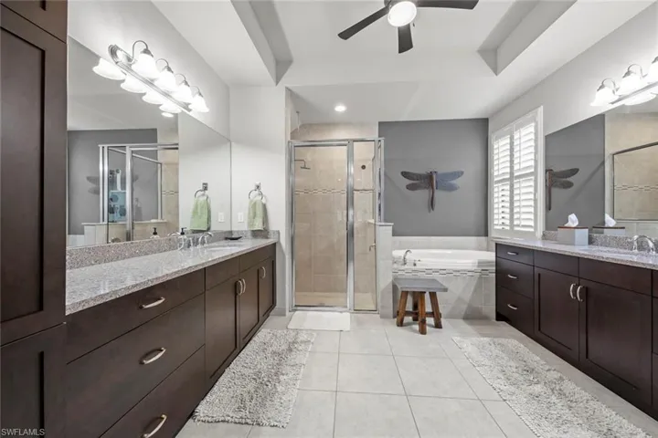 Primary bath with a shower and soaking tub, raised ceiling, two vanities, a sink, and tile patterned flooring