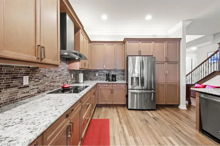 Kitchen with stainless steel appliances, wall range hood, backsplash, light wood finished floors, and crown molding