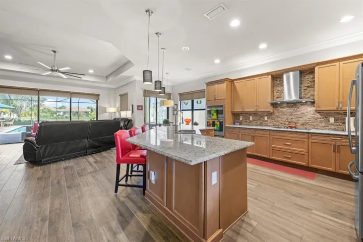 Kitchen featuring tasteful backsplash, wall  exhaust hood, open floor plan, wood finished floors, and stainless steel oven/microwave