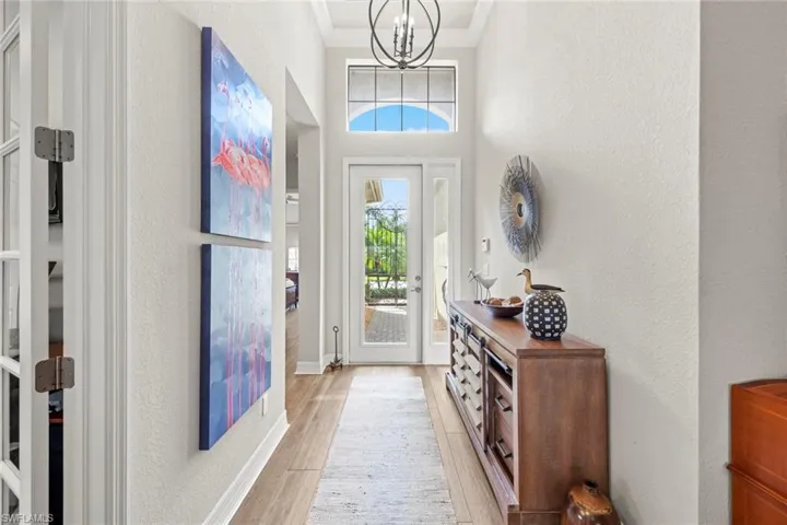 Foyer featuring baseboards, a textured wall, ornamental molding, light wood-style floors, and a notable chandelier