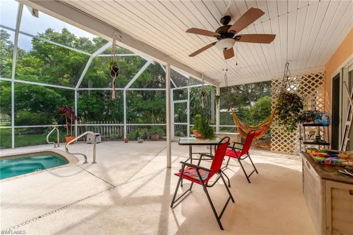 View of patio featuring a lanai, a ceiling fan, a sunroom, an outdoor pool, and view of scattered trees