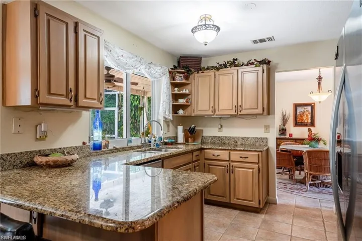 Kitchen featuring a peninsula, light stone counters, stainless steel refrigerator with ice dispenser, open shelves, and light tile patterned floors
