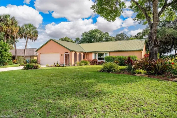 Ranch-style house with stucco siding, driveway, a front yard, a garage, and a metal roof