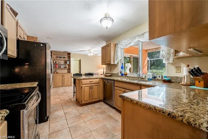 Kitchen featuring appliances with stainless steel finishes, dark stone counters, light brown cabinets, and light tile patterned flooring