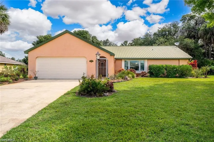 Single story home featuring a metal roof, stucco siding, a garage, driveway, and a front yard