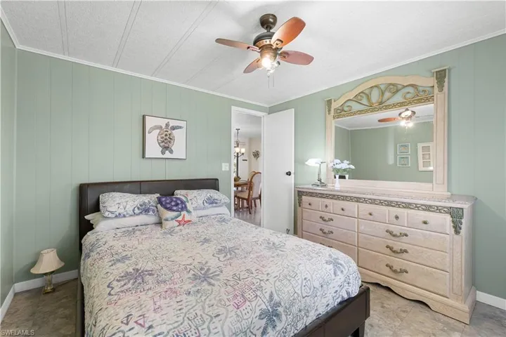 Bedroom with ceiling fan, wooden walls, crown molding, and a textured ceiling