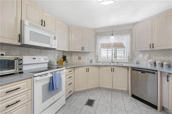 Kitchen with light tile patterned floors, white appliances, backsplash, and sink