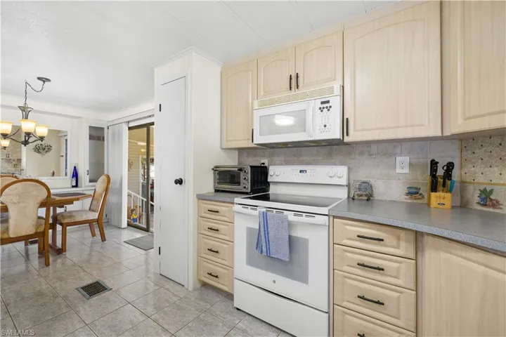 Kitchen with light brown cabinets, pendant lighting, white appliances, and a notable chandelier