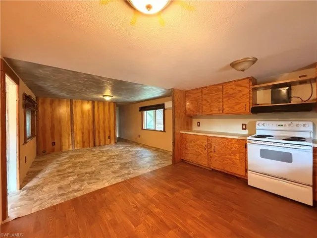 Kitchen with white electric range, light countertops, open floor plan, wood finish cabinetry, and a textured ceiling