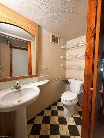 Bathroom featuring a textured wall, a textured ceiling, and light flooring