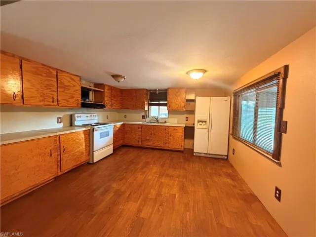 Kitchen with white appliances, light countertops, wood finish cabinetry, and dark wood-style floors